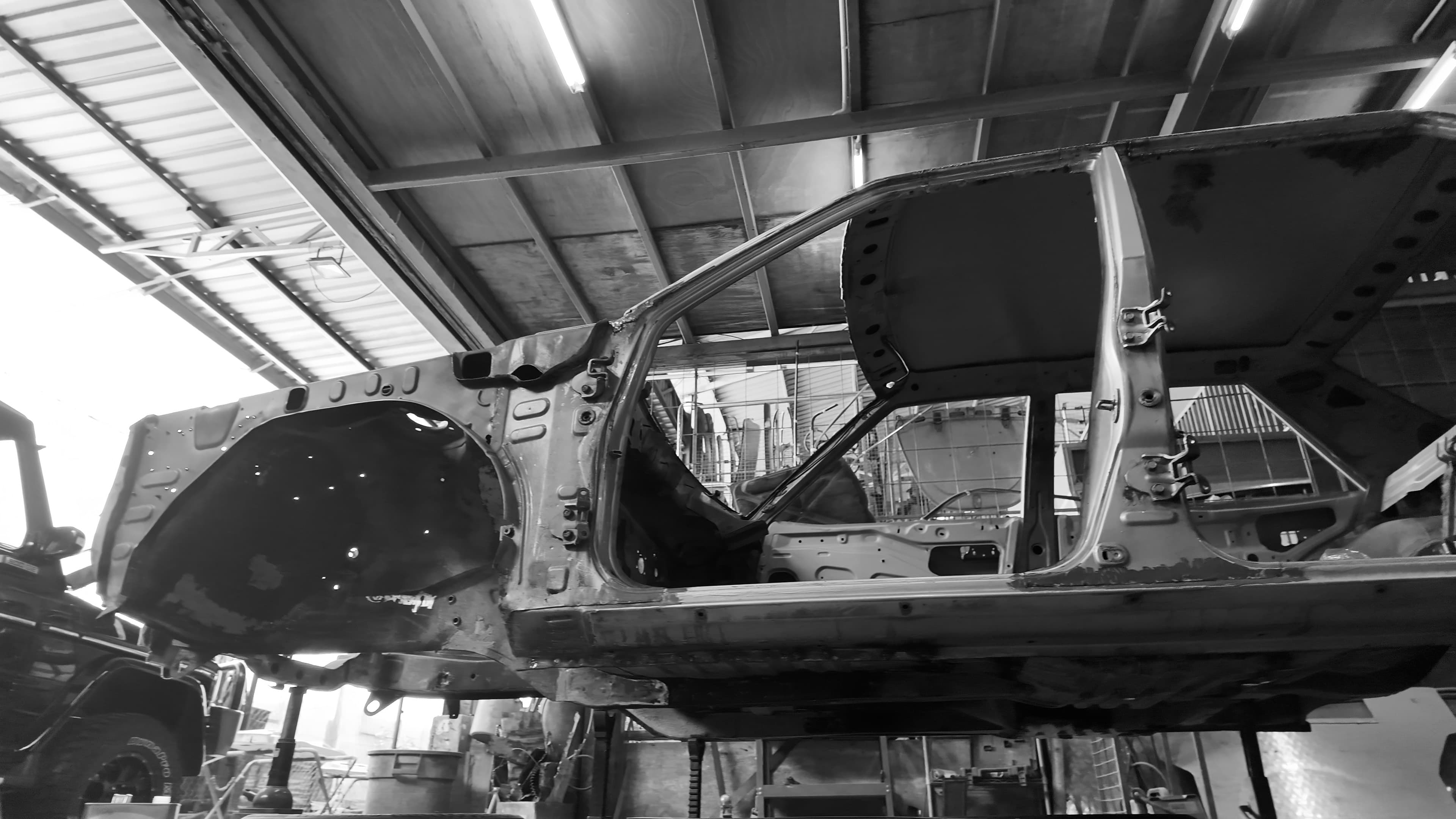 A stripped car shell on a lift in a workshop, down to bare metal