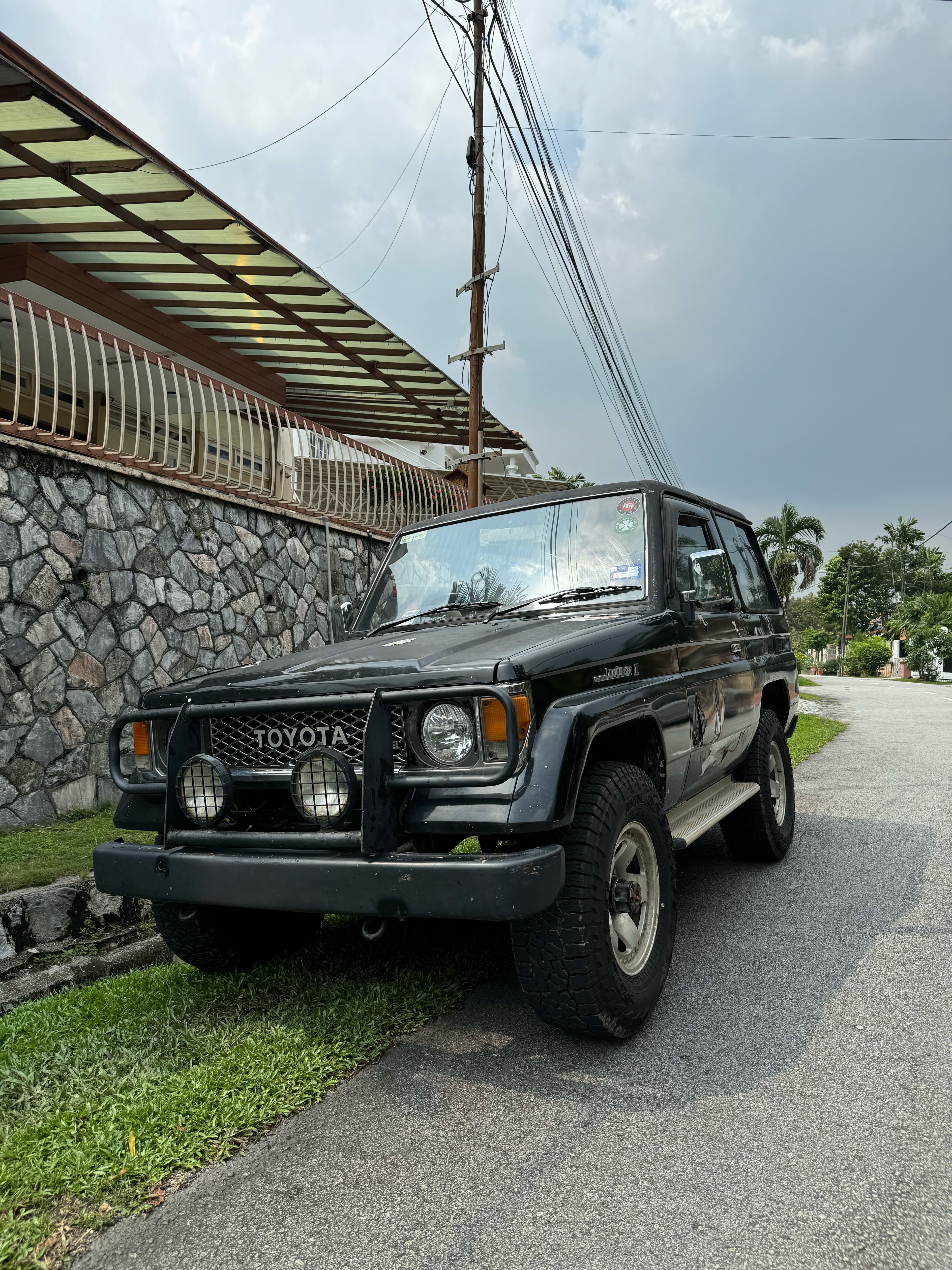 A black Toyota Land Cruiser II with a bull bar and spotlights, parked on a residential street